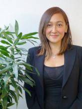 Woman with long brown hair sitting next to a plant and smiling