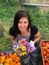 Vanessa kneeling in the grass holding flowers and smiling.